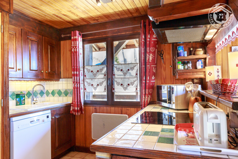 Cuisine avec fenêtre. Deux plans : côté évier, lave-vaisselle et lave-linge dans l'armoire, en face le côté cuisson